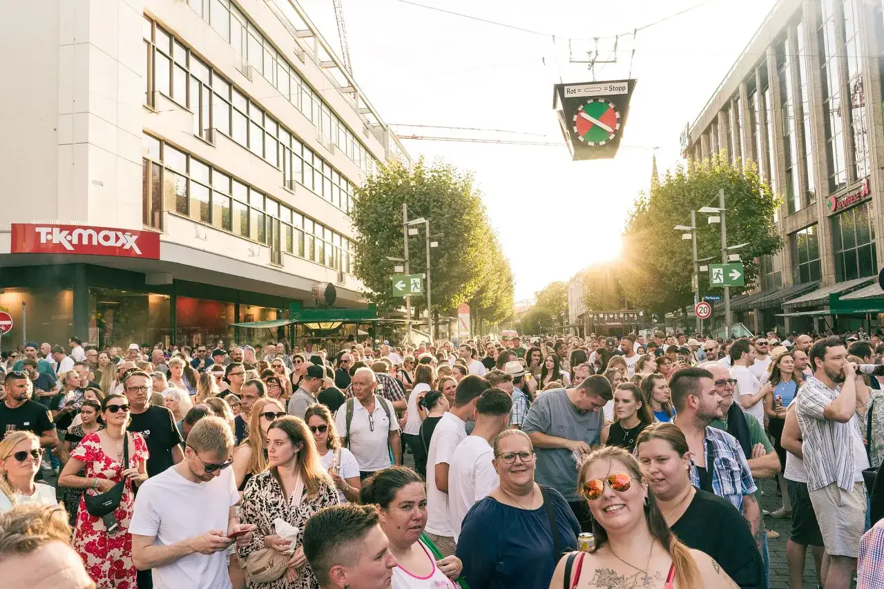 Menschenmenge feiert bei kostenlosen Veranstaltungen in Bochum. Die Sonne scheint, ein Verkehrssignal hängt über der Straße.