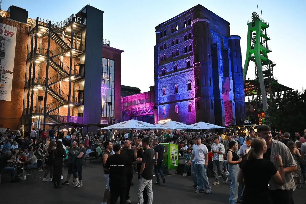 Menschen feiern auf einem Industriegel&auml;nde, beleuchtet von bunten Lichtern. Ein lebendiges Fest an besonderen Extraschicht Spielorten.