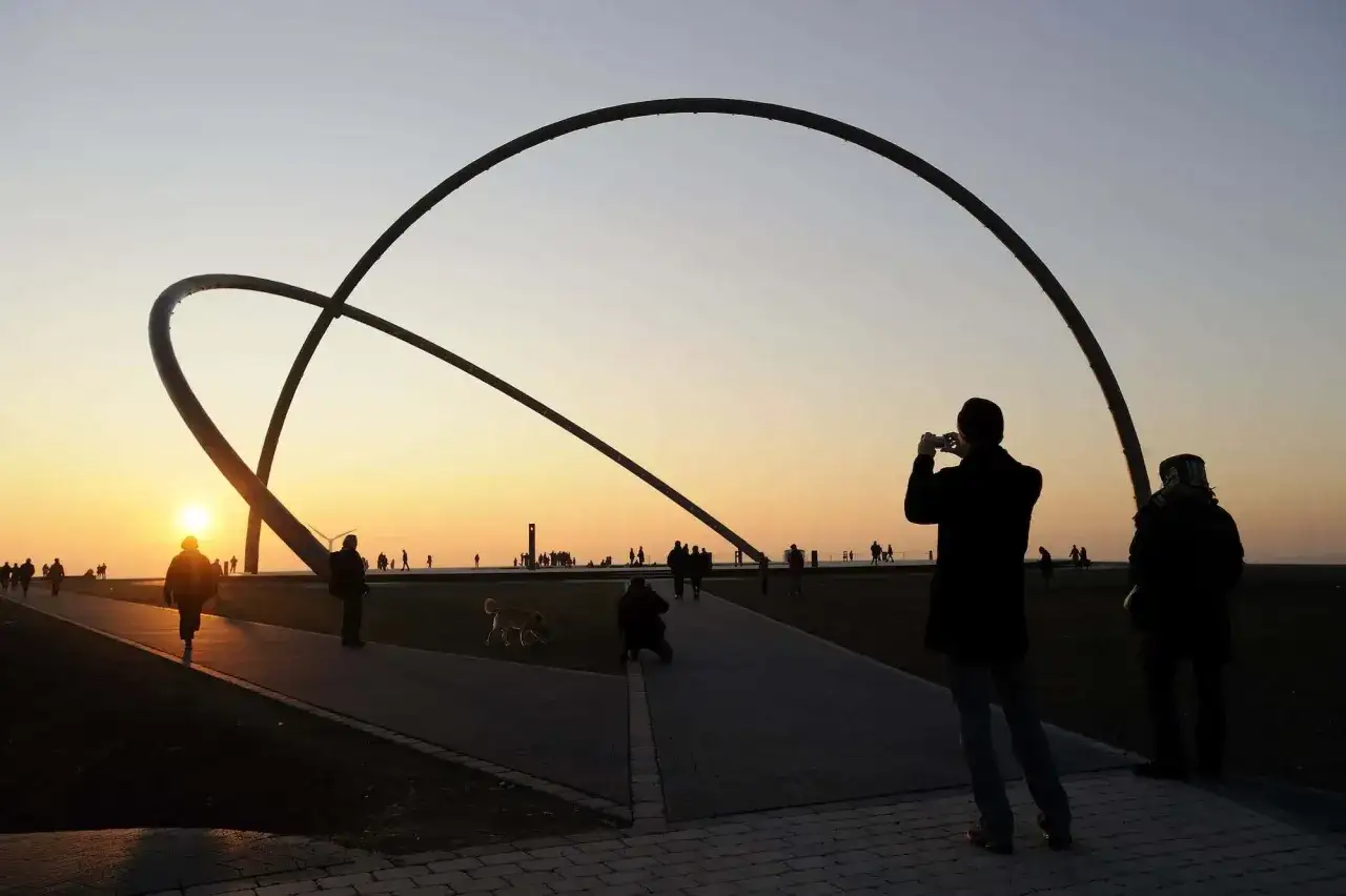 Sonnenuntergang am Halde Rungenberg Parken. Menschen spazieren unter riesigen Stahlb&ouml;gen, ein Fotograf h&auml;lt den Moment fest.