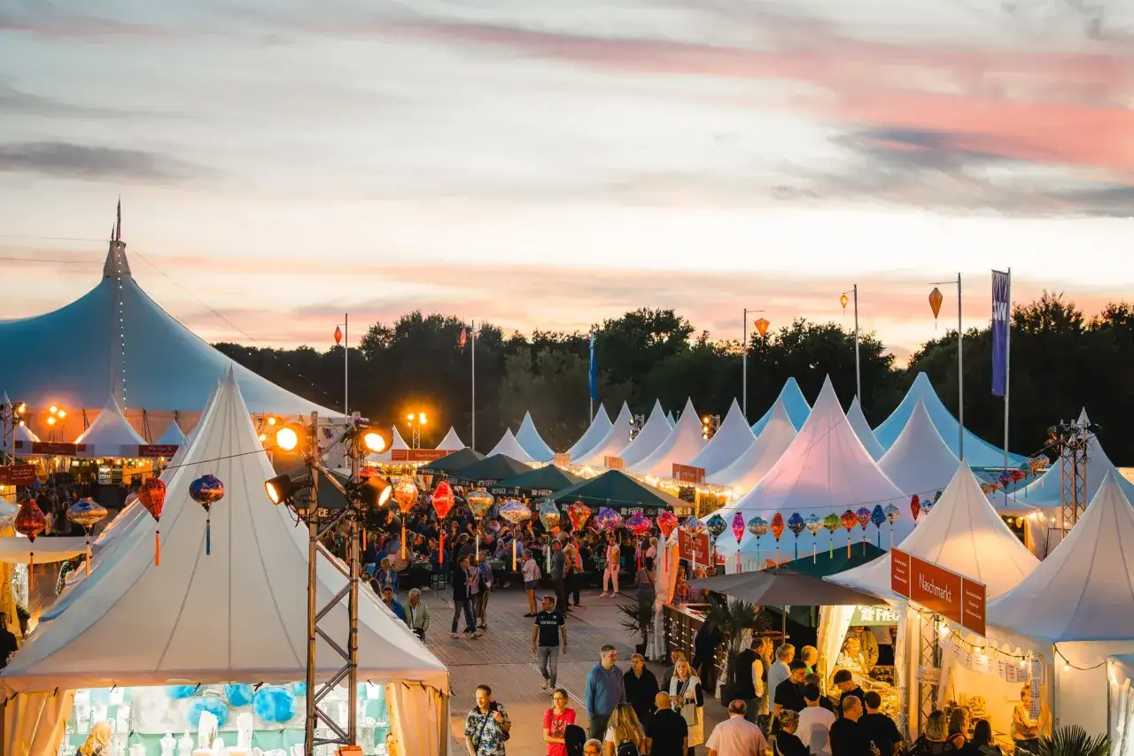 Buntes Treiben bei Veranstaltungen im Ruhrgebiet: Zelte, Lichterketten und bunte Lampions beleuchten einen belebten Markt bei Sonnenuntergang.
