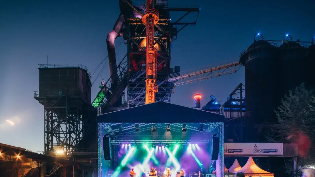 Bühne mit Band vor Industriekulisse bei Festivals NRW. Bunte Lichter beleuchten die Nacht.