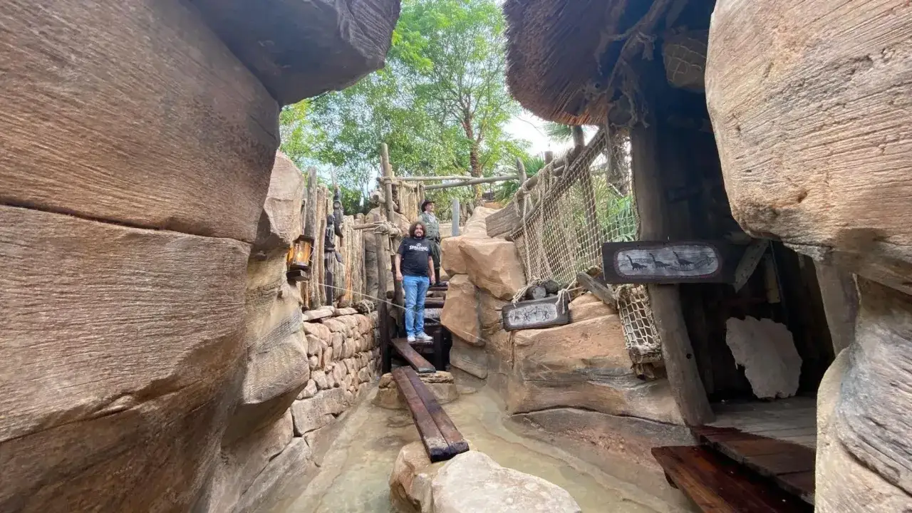 Ein Mann steht auf einem Holzsteg im Phantasialand. Der Abenteuerpfad ist mit Felsen und Seilen gestaltet.