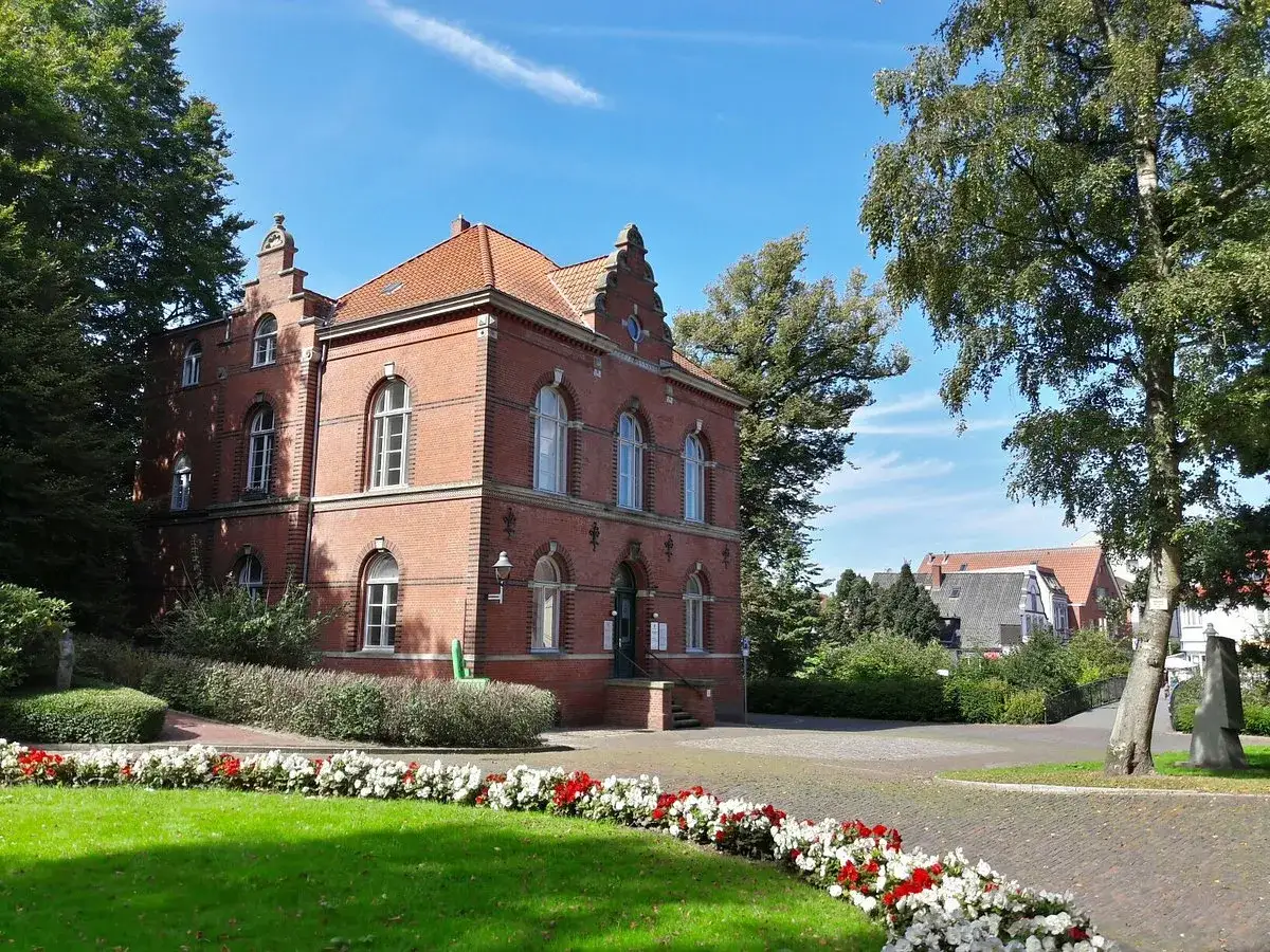 Ein Backsteingebäude in der Cuxhaven Altstadt, umgeben von Bäumen und Blumen.