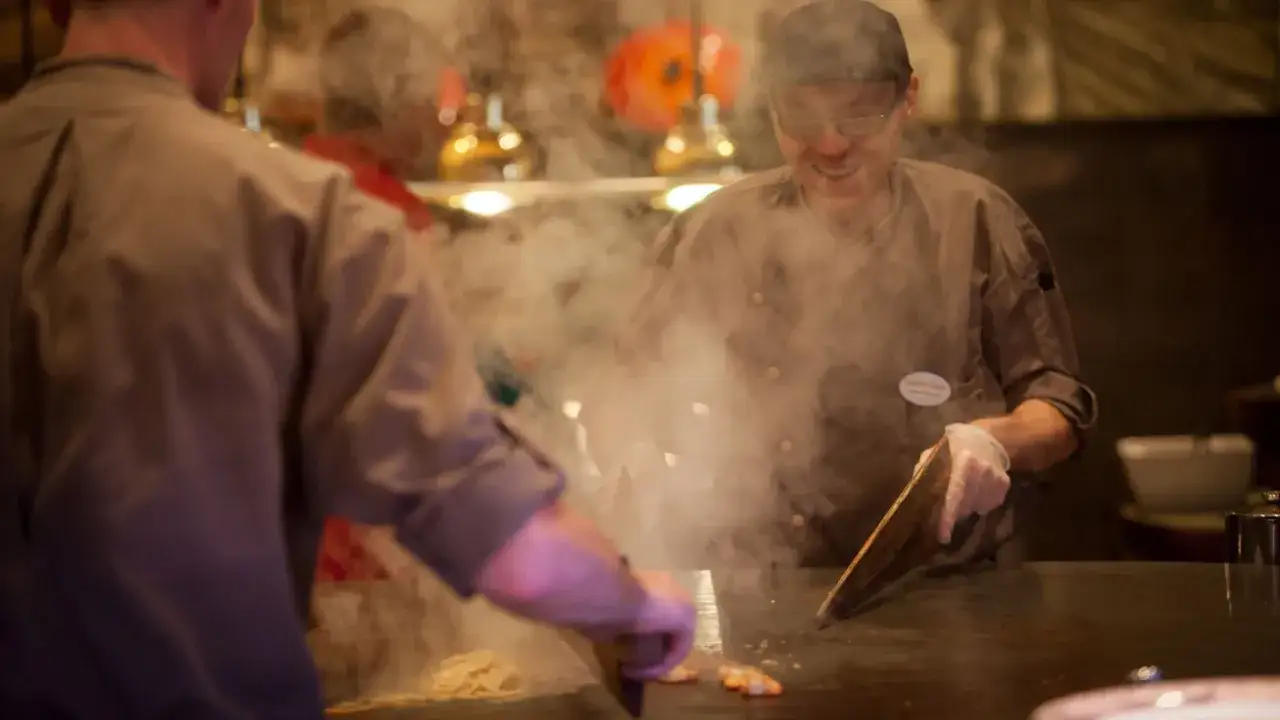 Köche bereiten im Bell Rock Buffet Speisen zu. Dampf steigt von der heißen Platte auf, während sie mit Werkzeugen arbeiten.