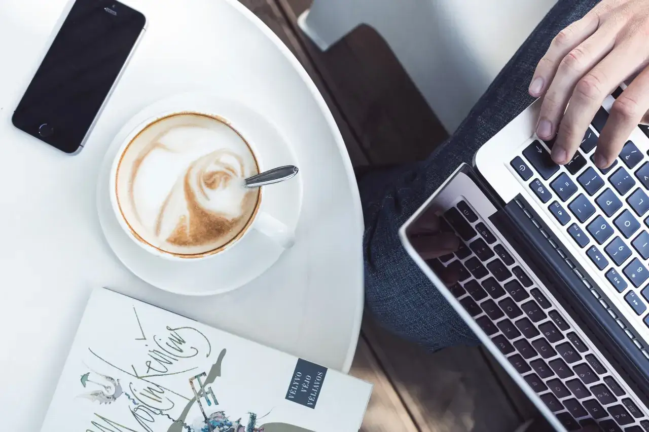 Person lernt im Café mit Laptop, Kaffee und Handy.