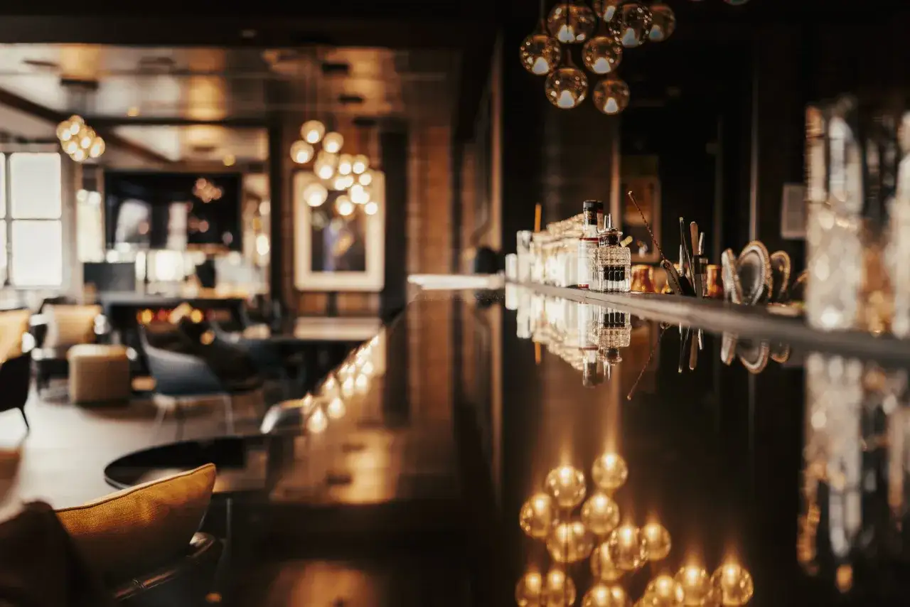 Ein stilvoller Bar-Bereich mit ged&auml;mpftem Licht und Spiegelungen. Flaschen und Gl&auml;ser stehen bereit, vielleicht f&uuml;r einen Oscar im Apropos-Cocktail.