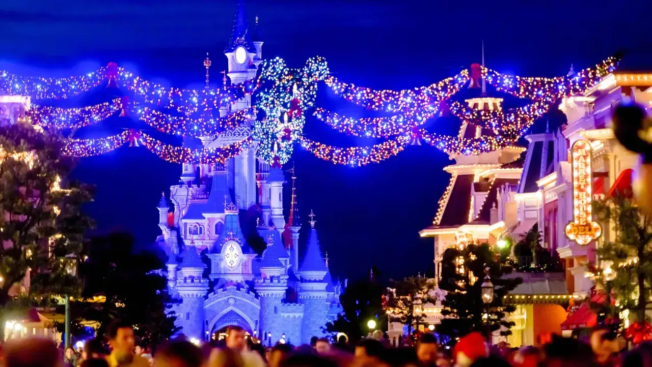 Magisches Disneyland Paris im Winter: Das Schloss leuchtet, Lichterketten schmücken die Gassen und Menschen genießen die festliche Atmosphäre.