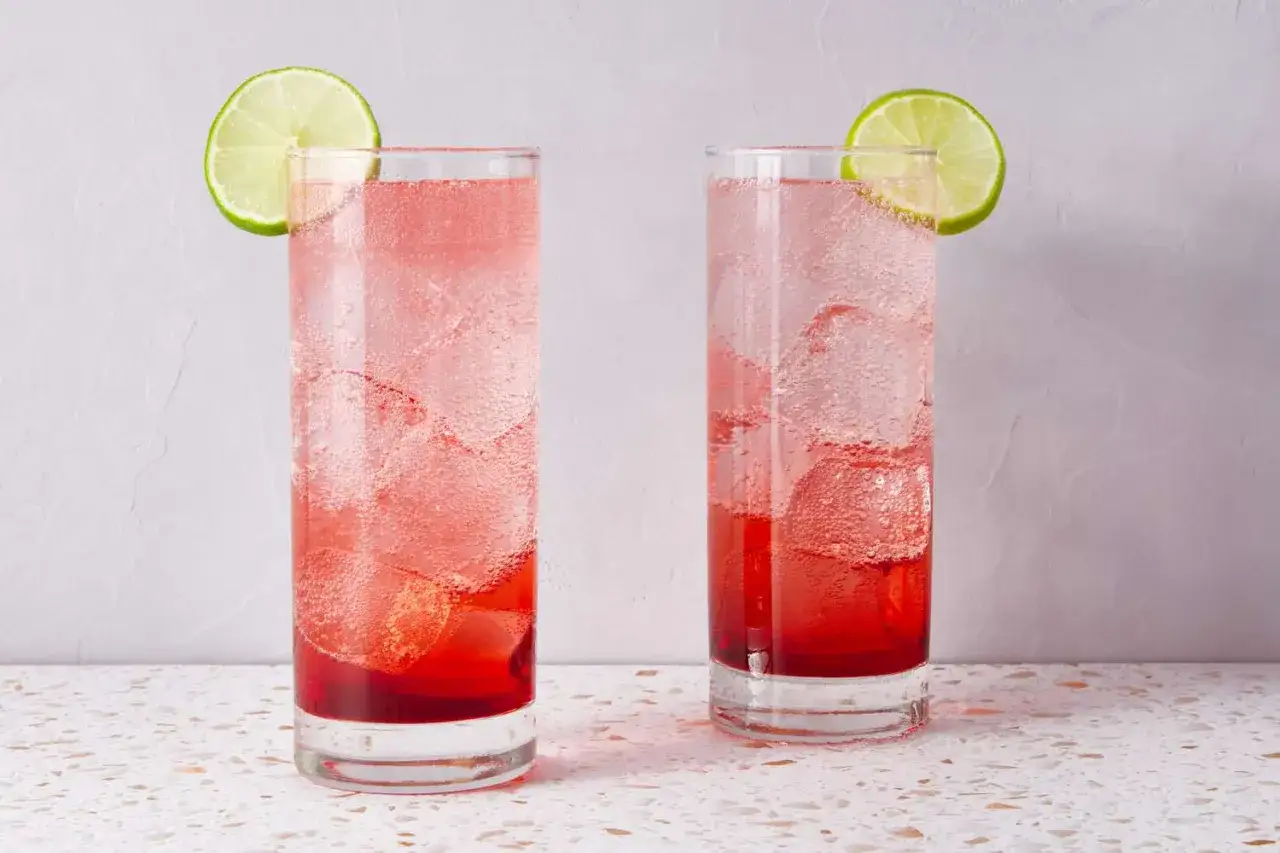 Zwei erfrischende Sommerdrinks mit Tonic Water und Limettenscheiben, gef&uuml;llt mit Eis und sprudelndem, rotem Getr&auml;nk.