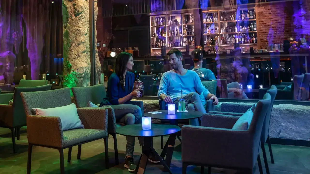 Ein Paar genie&szlig;t Getr&auml;nke in einer stilvollen Bar mit Felsformationen und ged&auml;mpftem Licht. Ein perfekter Ort f&uuml;r ein romantisches rulantica essen.