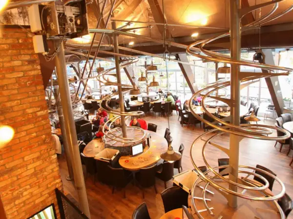 Einzigartiges Restaurant im Europa-Park mit Achterbahn-Schienen als Deko. Gäste sitzen an runden Tischen unter den metallischen Kurven.