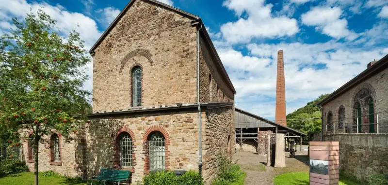 Altes rheinisches Bergwerk mit Backsteinkamin und einem Baum mit roten Beeren.
