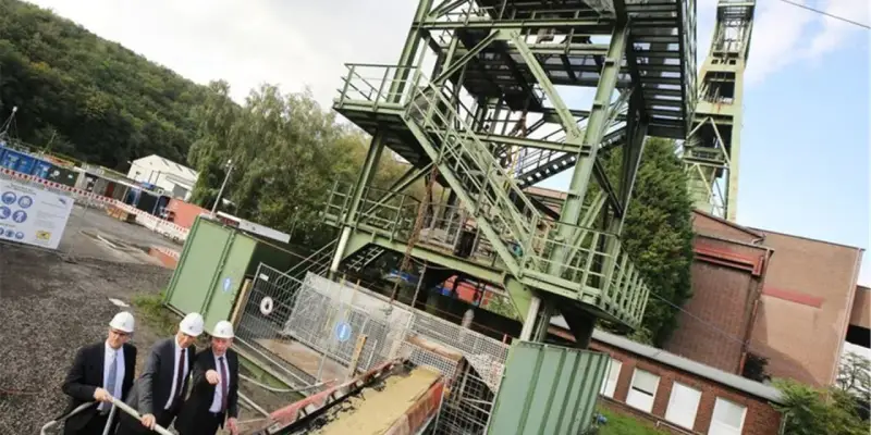 Drei Männer in Anzügen und Schutzhelmen inspizieren das Gelände der Zeche Bottrop. Ein Förderturm ragt in den Himmel.