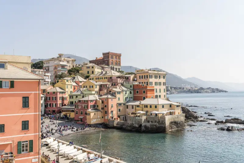 Bunte Häuserfronten am Meer in Genua, Italien. Boote liegen am Ufer, Menschen entspannen sich am Strand.