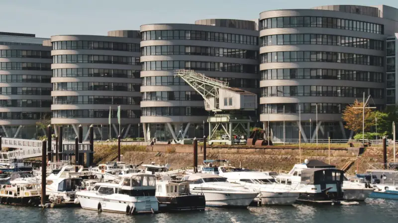 Moderne Gebäude am Duisburg Innenhafen mit vielen Yachten im Wasser. Ein alter Kran erinnert an die industrielle Vergangenheit.