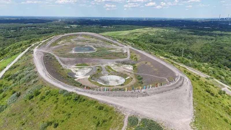 Die Halde Haniel mit ihrem Amphitheater und bunten Stelen, umgeben von grüner Natur und Windrädern in der Ferne.