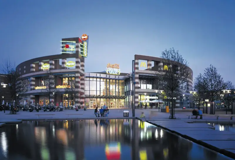 Abendstimmung am Centro Oberhausen. Die beleuchtete Fassade mit den Logos von McDonald's und Coca-Cola spiegelt sich im Wasser.