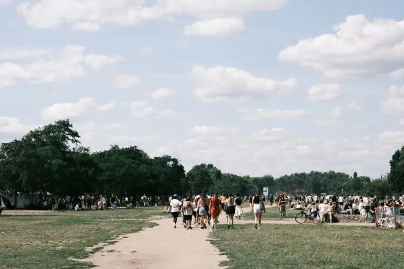 Menschen strömen über eine Wiese, unter Bäumen und Zelten. Ein sonniger Tag, wo ist Pfingsten was los?